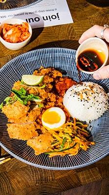 guest pours amai sauce over rice served with crisy sambal fried chicken