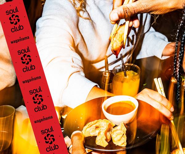 a guest holds a single gyoza in chopsticks above a ramekin of hoisin sauce, on a black plate with 3 more gyoza