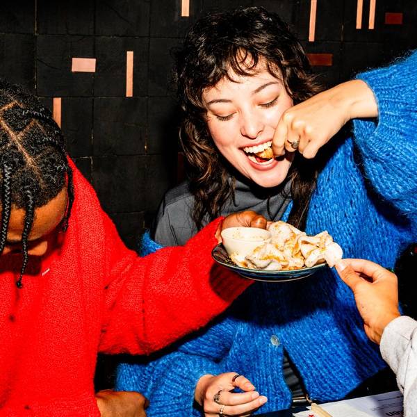 a guy in a red jumper holds a plate of prawn crakers in front of a similng woman in a blue jumper who is biting down on a cracker